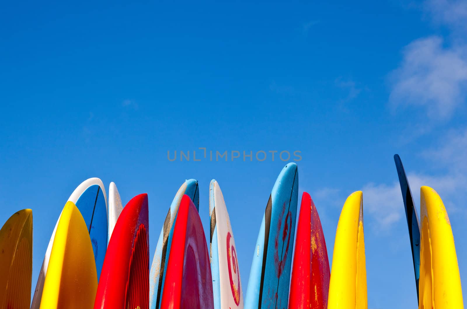 Set of different color surf boards in a stack by ocean