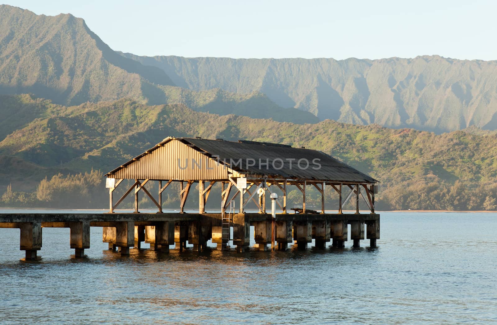 Rising sun illuminates the Hanalei pier and Na Pali mountains in Kauai