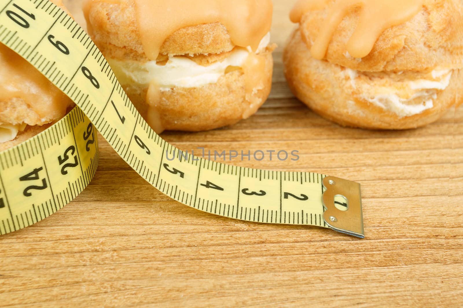 concept of slimming, closeup of caramel cakes with measuring tape on desk