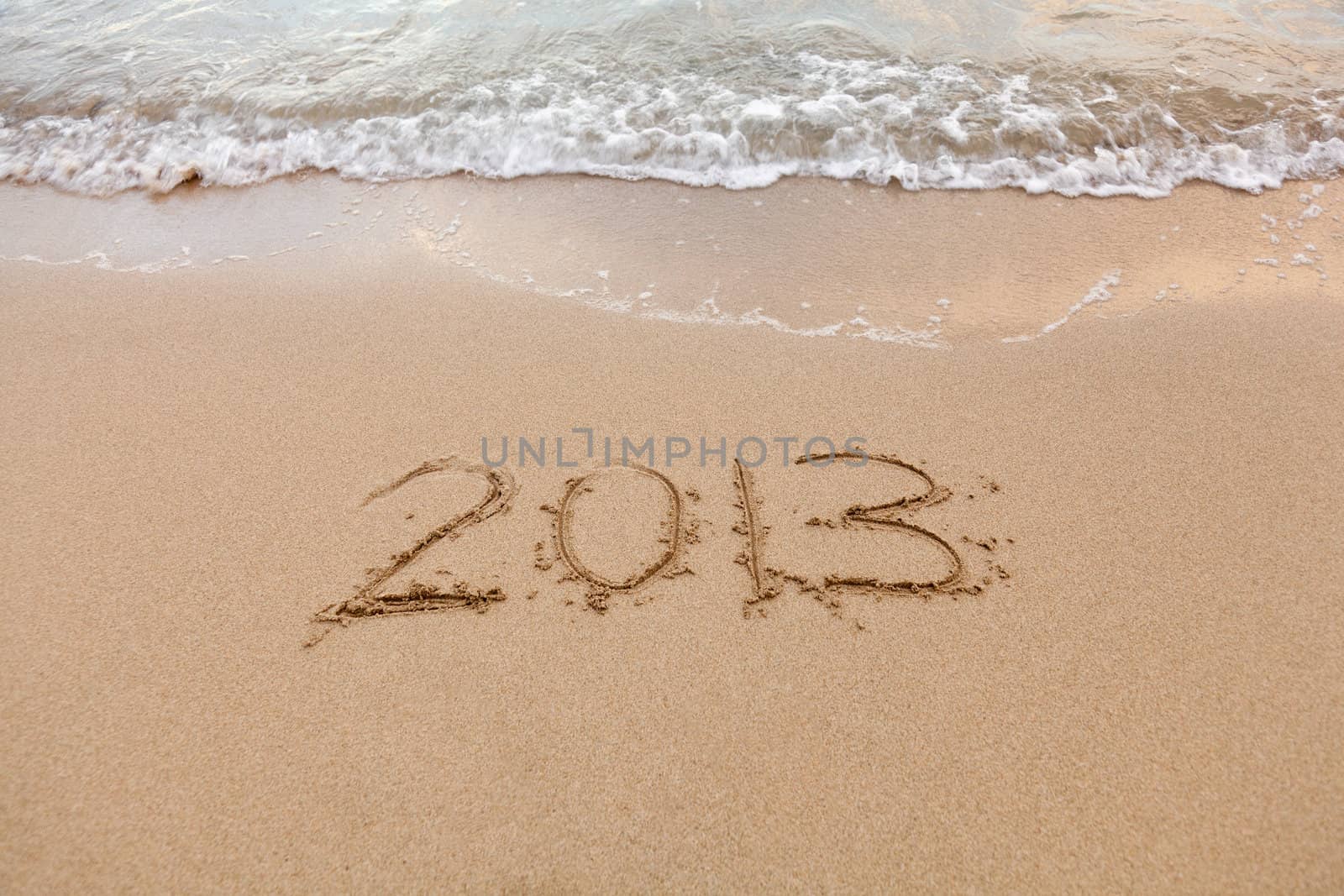 2013 written in sand on beach with sea waves starting to erase the word