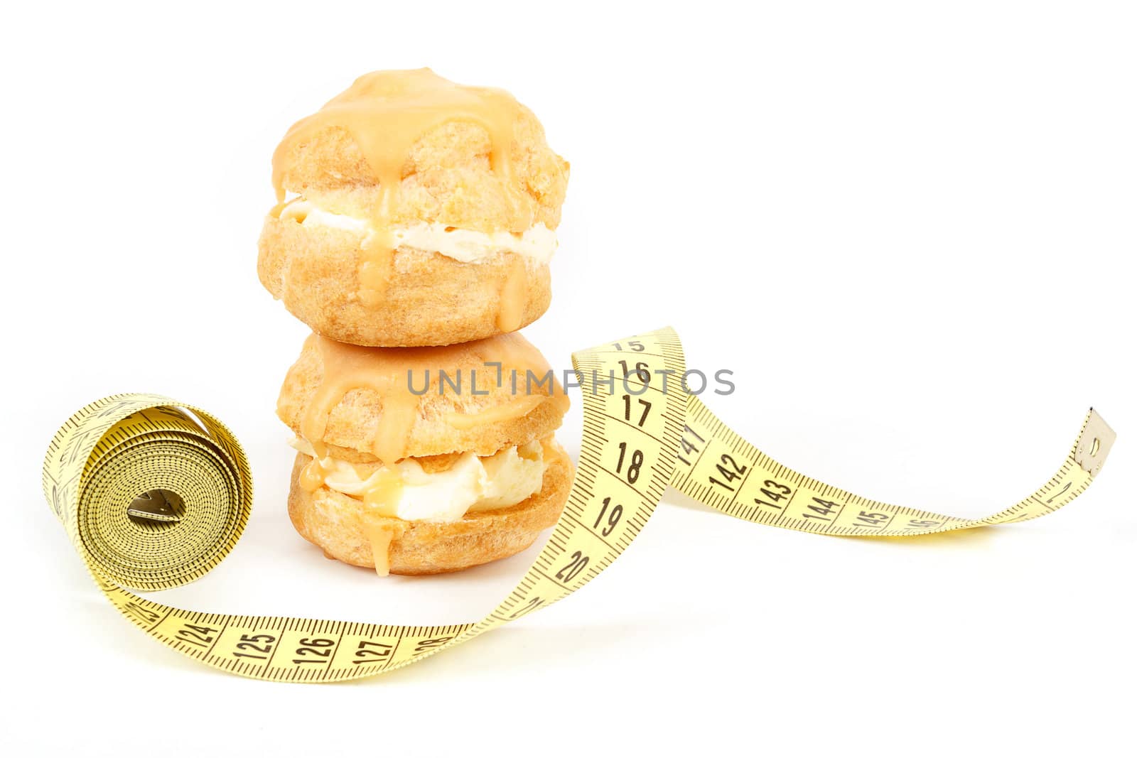 concept of slimming, caramel cakes with measuring tape on white background