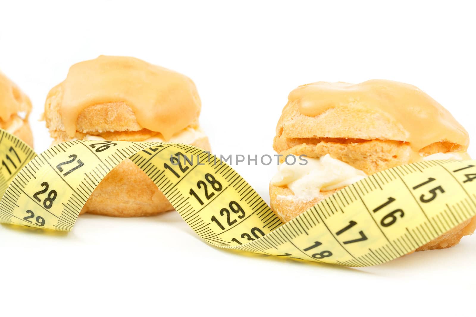 concept of slimming, caramel cakes with measuring tape on white background