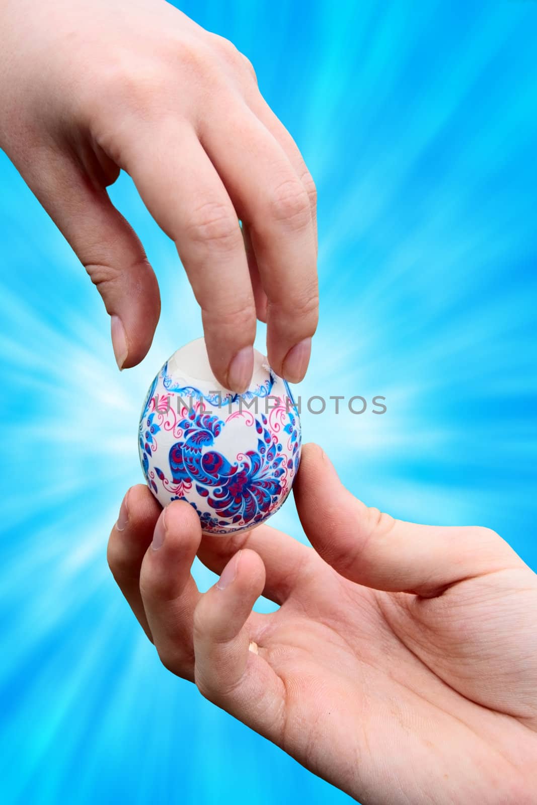 male hand giving easter colored egg to woman hand over blue background