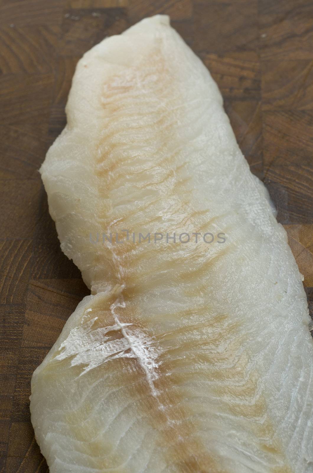 Close up of fresh raw cod fillet on a wood cutting board