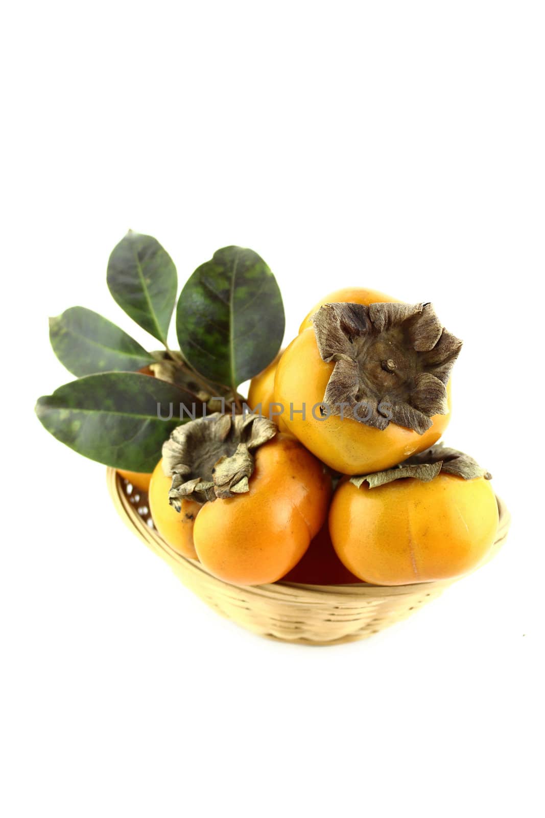 Set of persimmon fruit with leaves in straw basket.