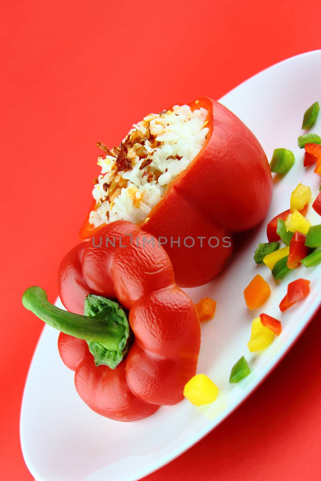 Stuffed red pepper in a dish on red background .