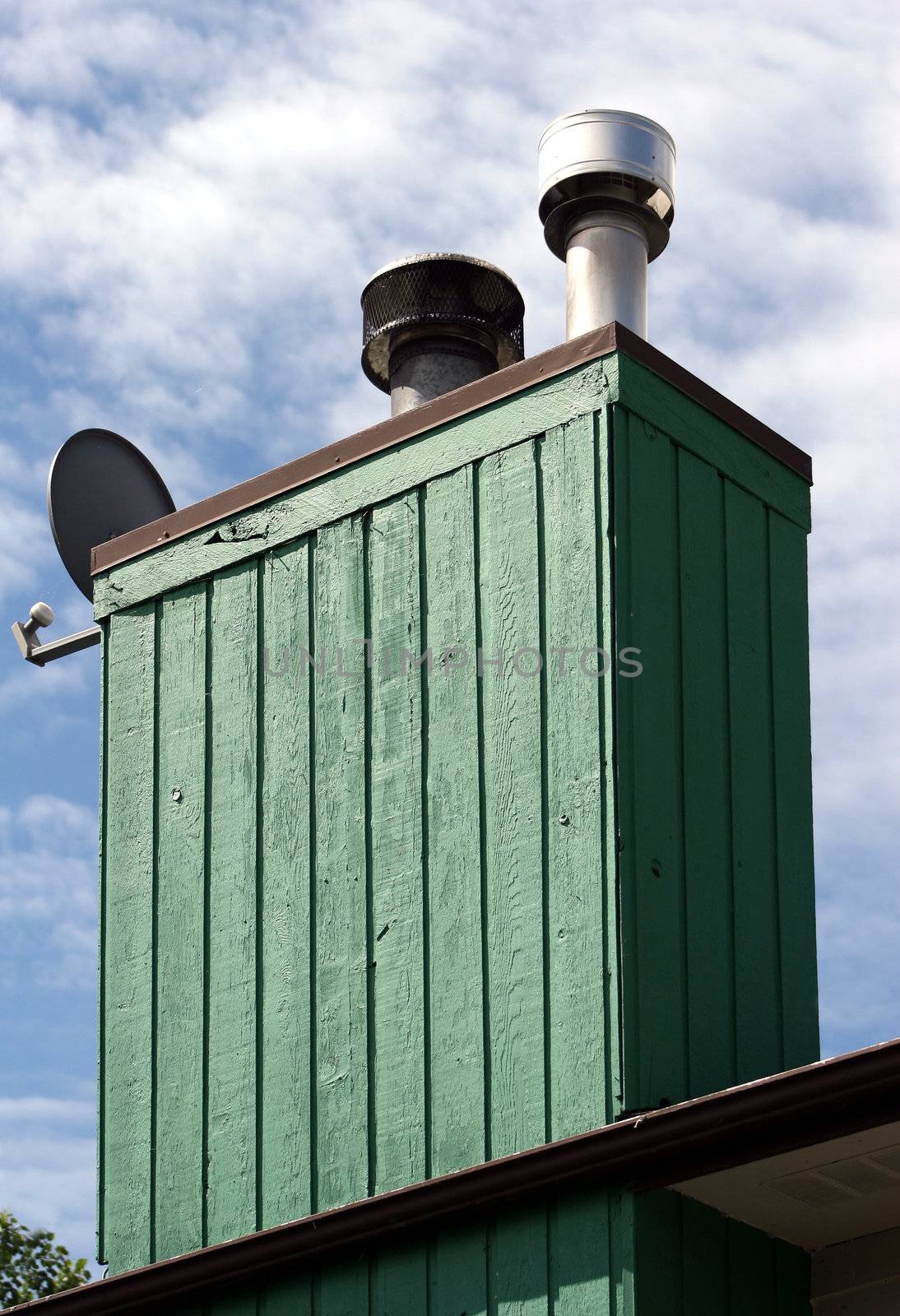 A green wooden chimney on a home with sky in the background