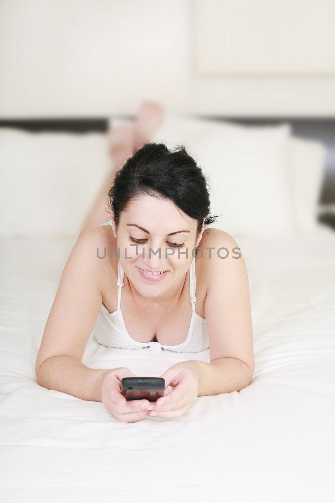 Happy female teenager using cellphone lying on the bed against w by dacasdo
