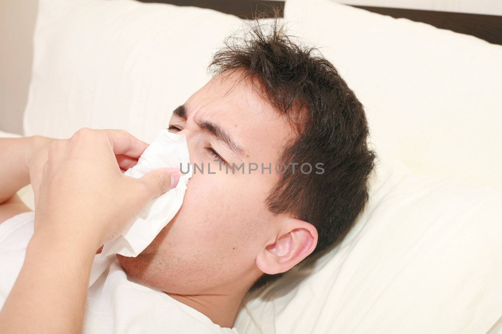 Sick man blowing his nose lying on his bed at morning