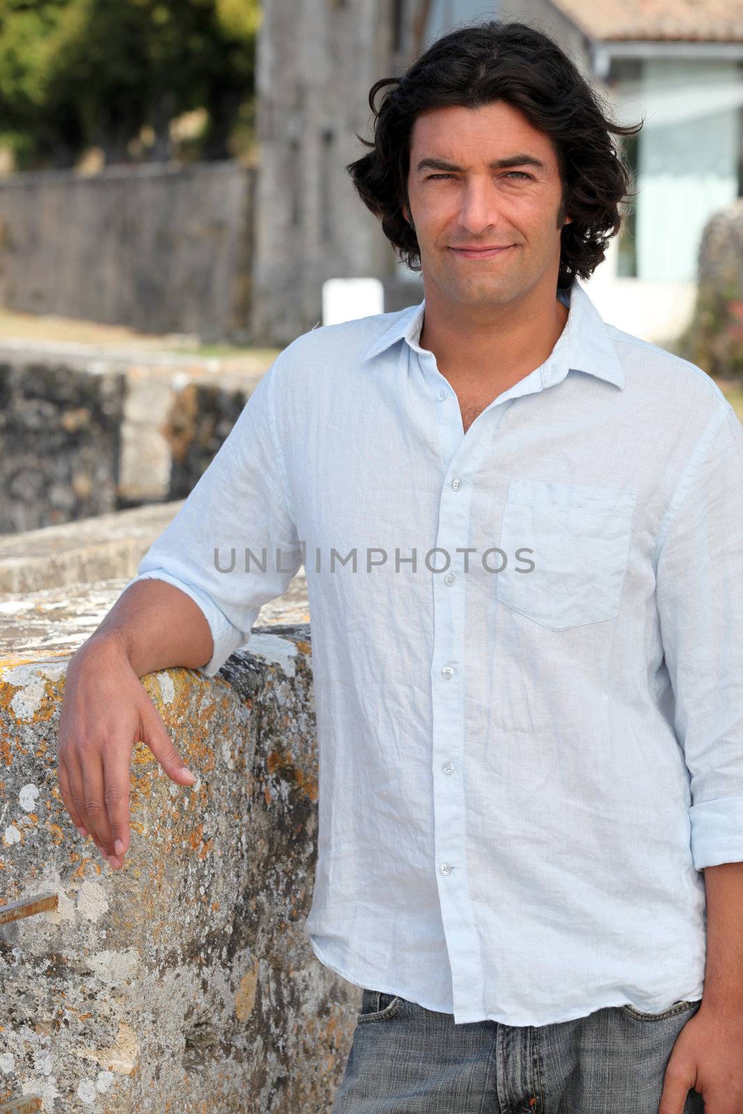 Man with long hair leaning on an old stone wall