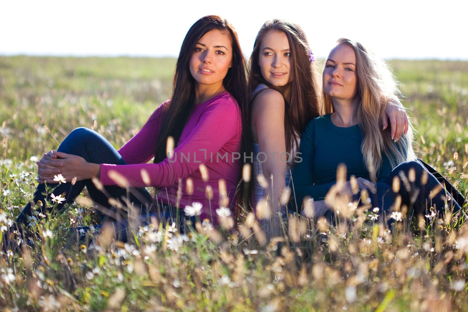 three young beautiful woman sitting in a field on the  sky backg by jannyjus
