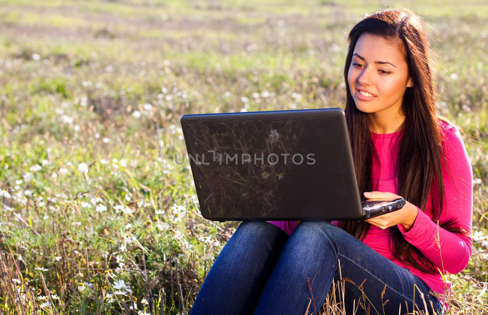 young beautiful woman with a laptop sitting in the field on sky background 