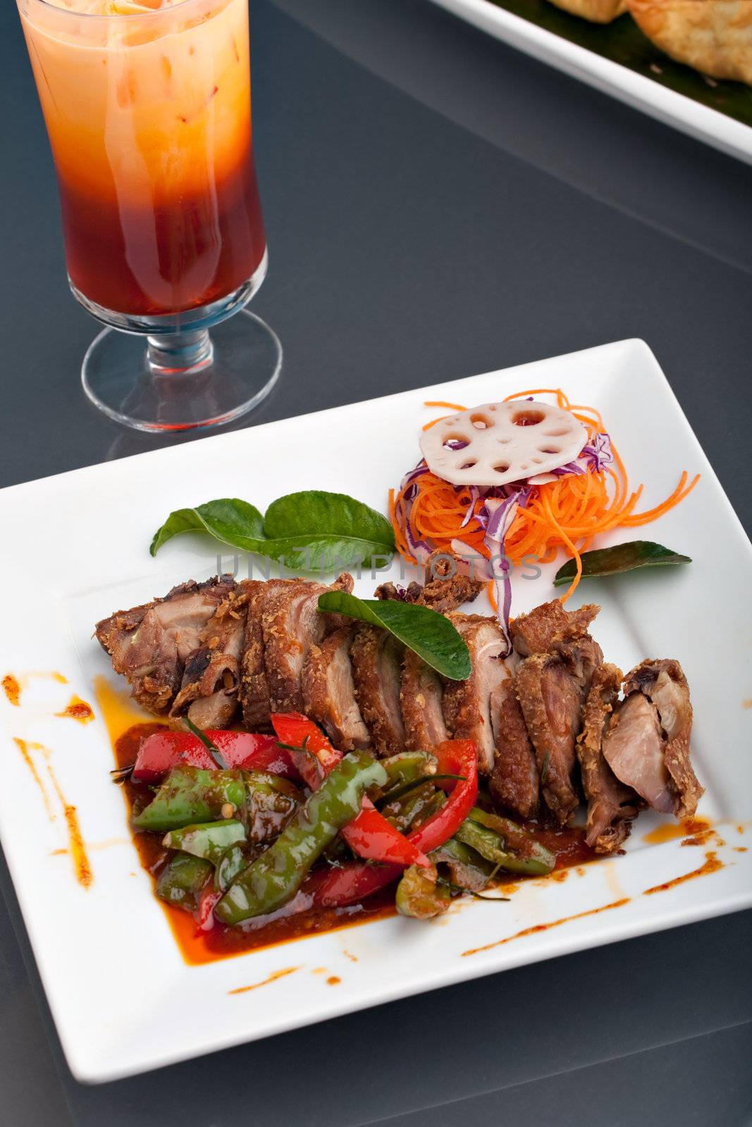 A beautifully presented dish of Thai style roast chile basil duck with mixed vegetables and thai iced tea.