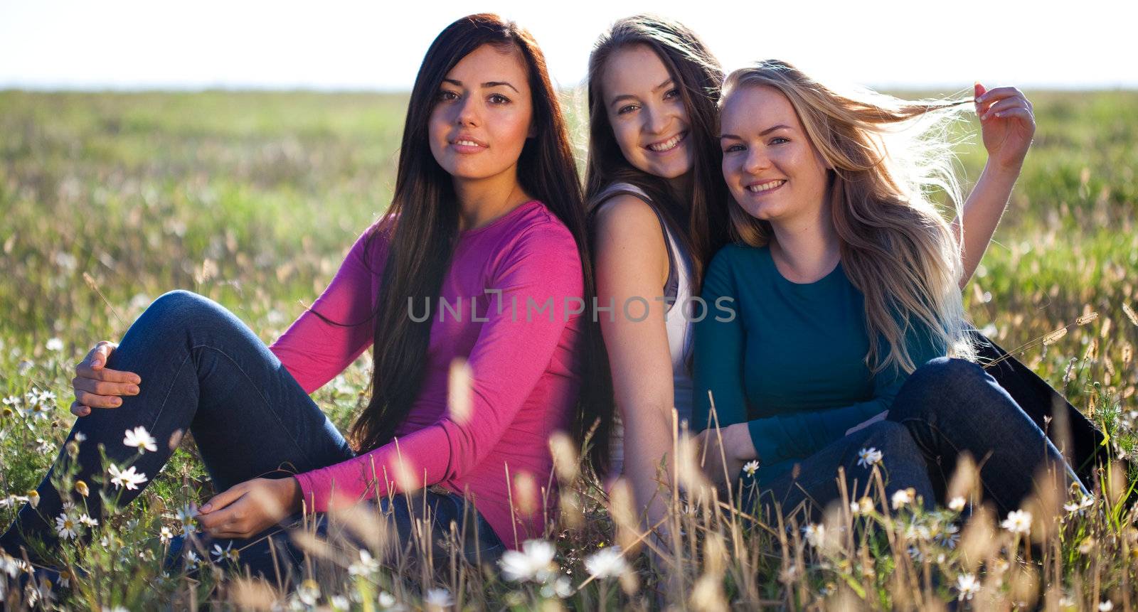 three young beautiful woman sitting in a field on the  sky backg by jannyjus