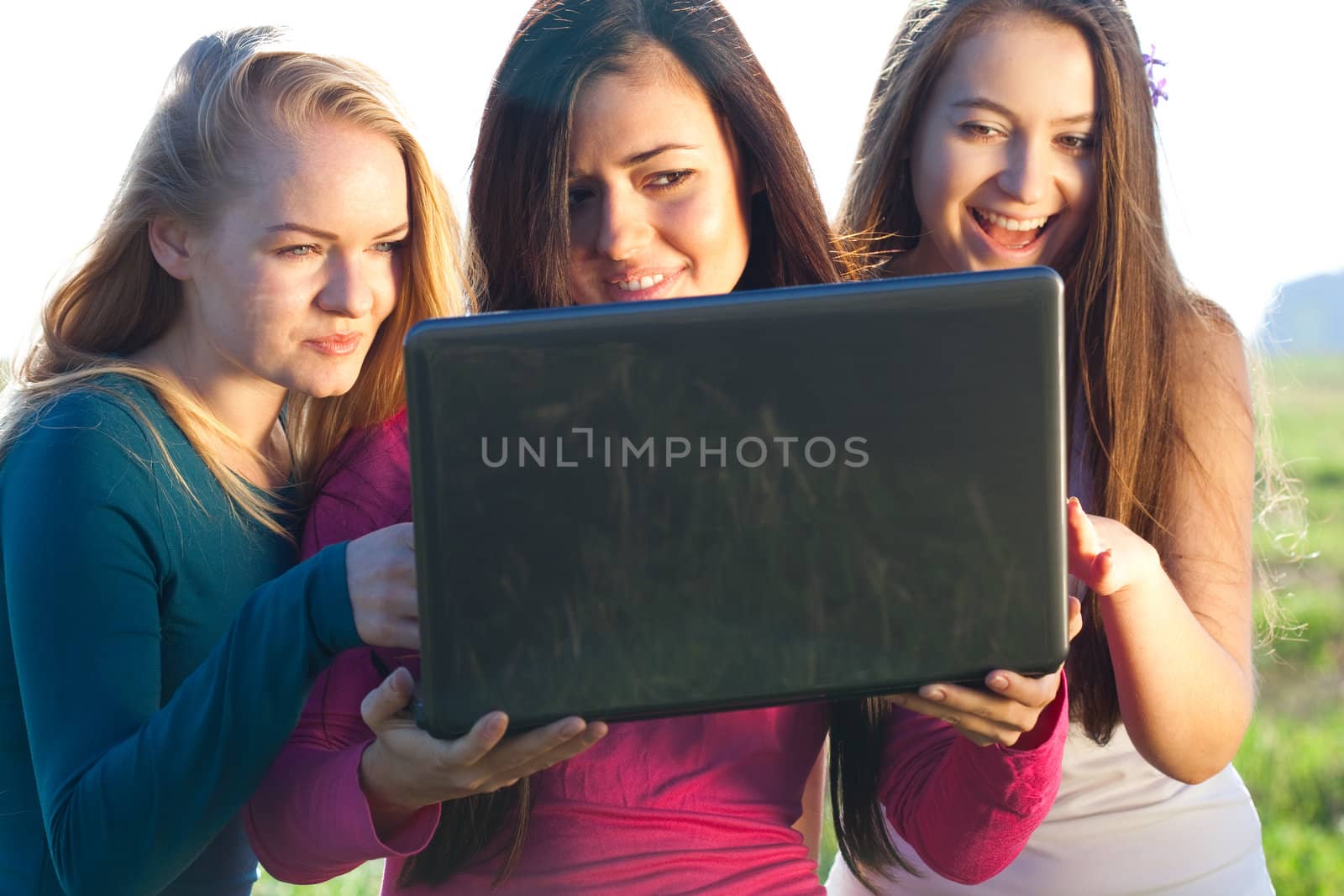 three young beautiful woman with a laptop in the field on sky ba by jannyjus