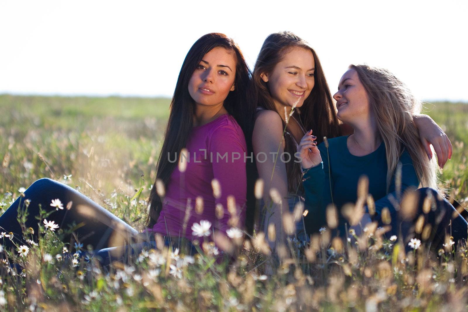 three young beautiful woman sitting in a field on the  sky backg by jannyjus