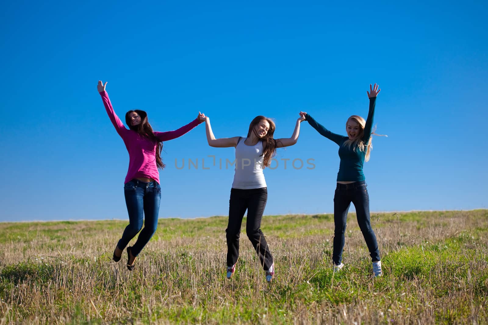 three young beautiful woman jumping into the field against the sky