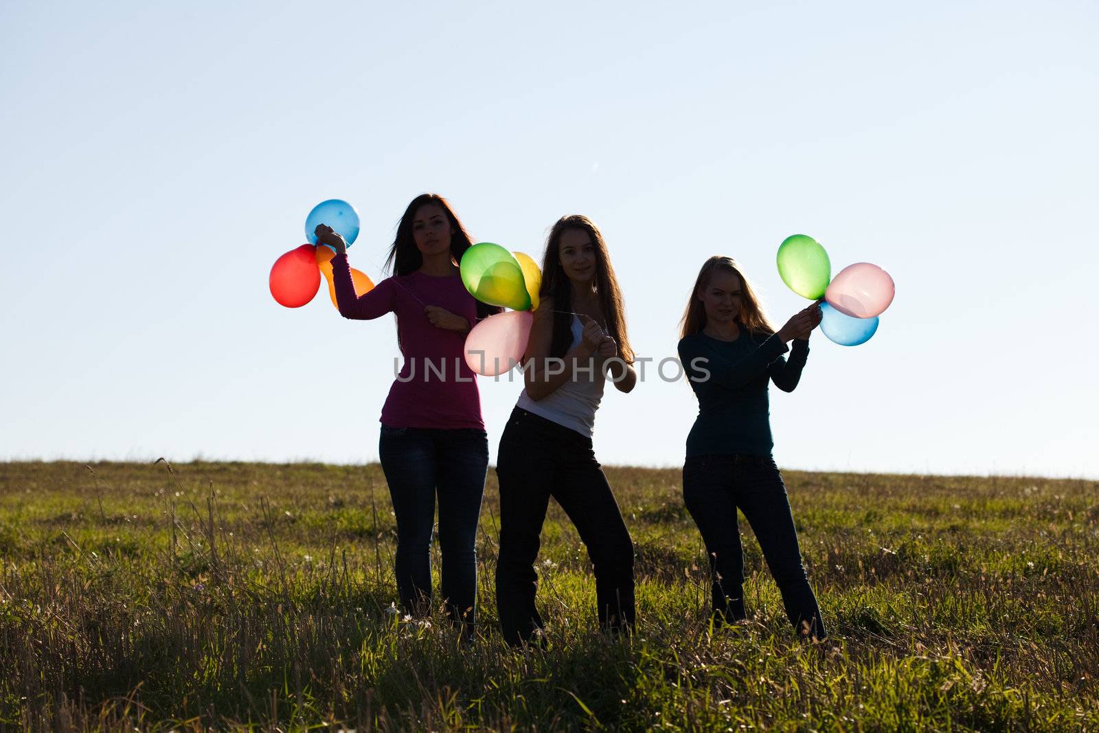 three young beautiful woman with balloons into the field against the sky