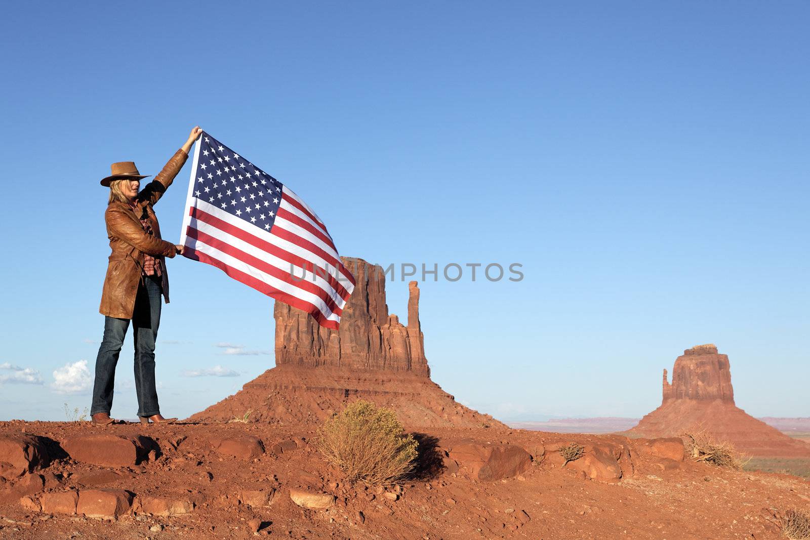 beautiful blond woman holding USA flag at Monument Valley
