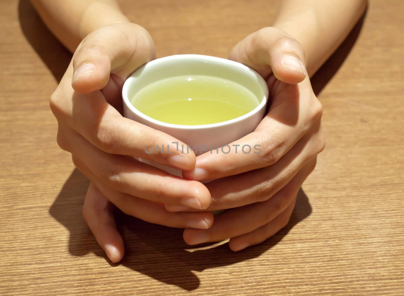Woman hands holding Japanese green teacup on table. 