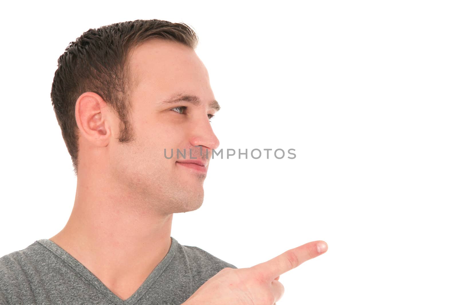 Smiling young man looking sideways towards centre frame and pointing with his finger to blank copy space isolated on white