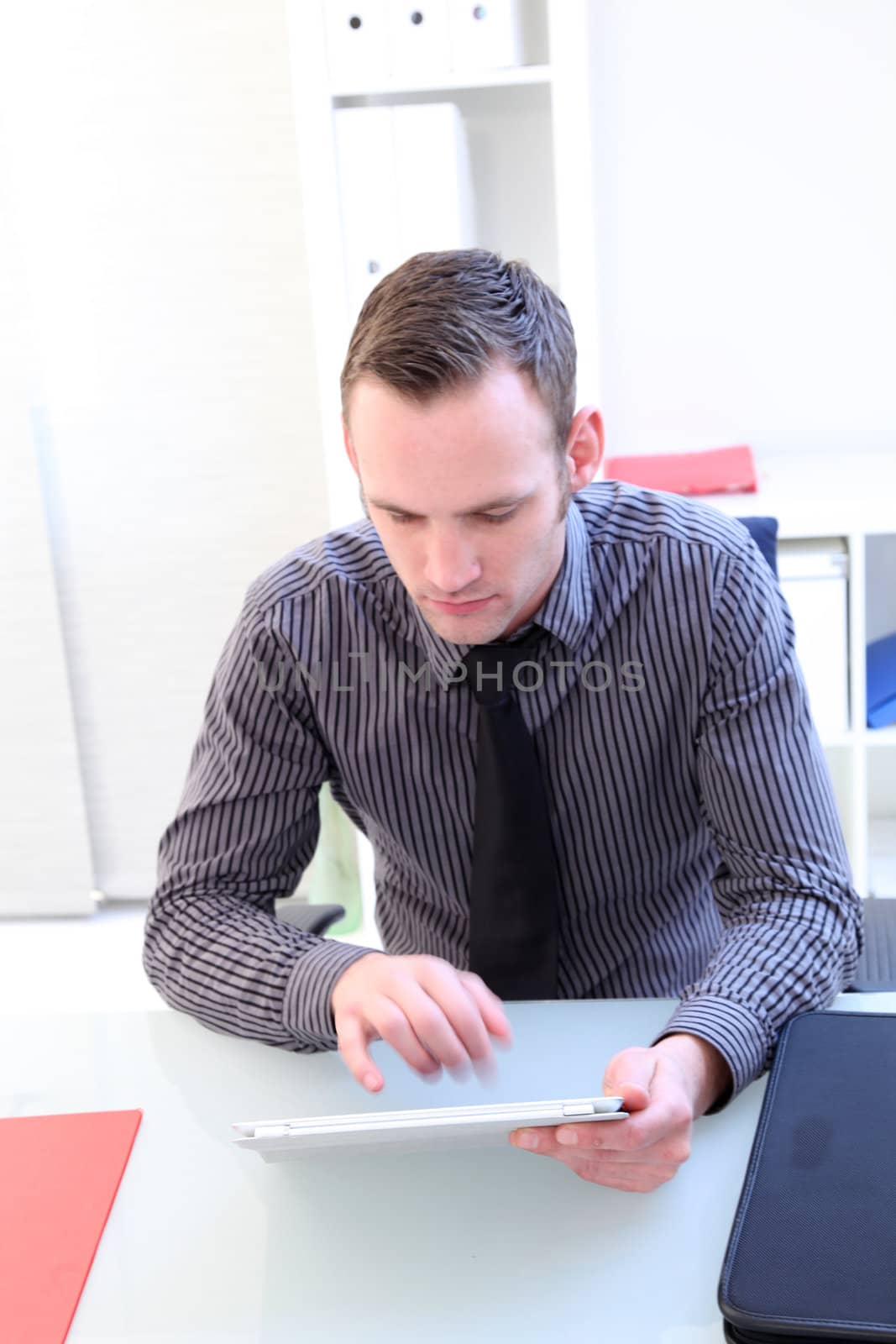 High angle view of a young businessman seated at his desk using a handheld tablet