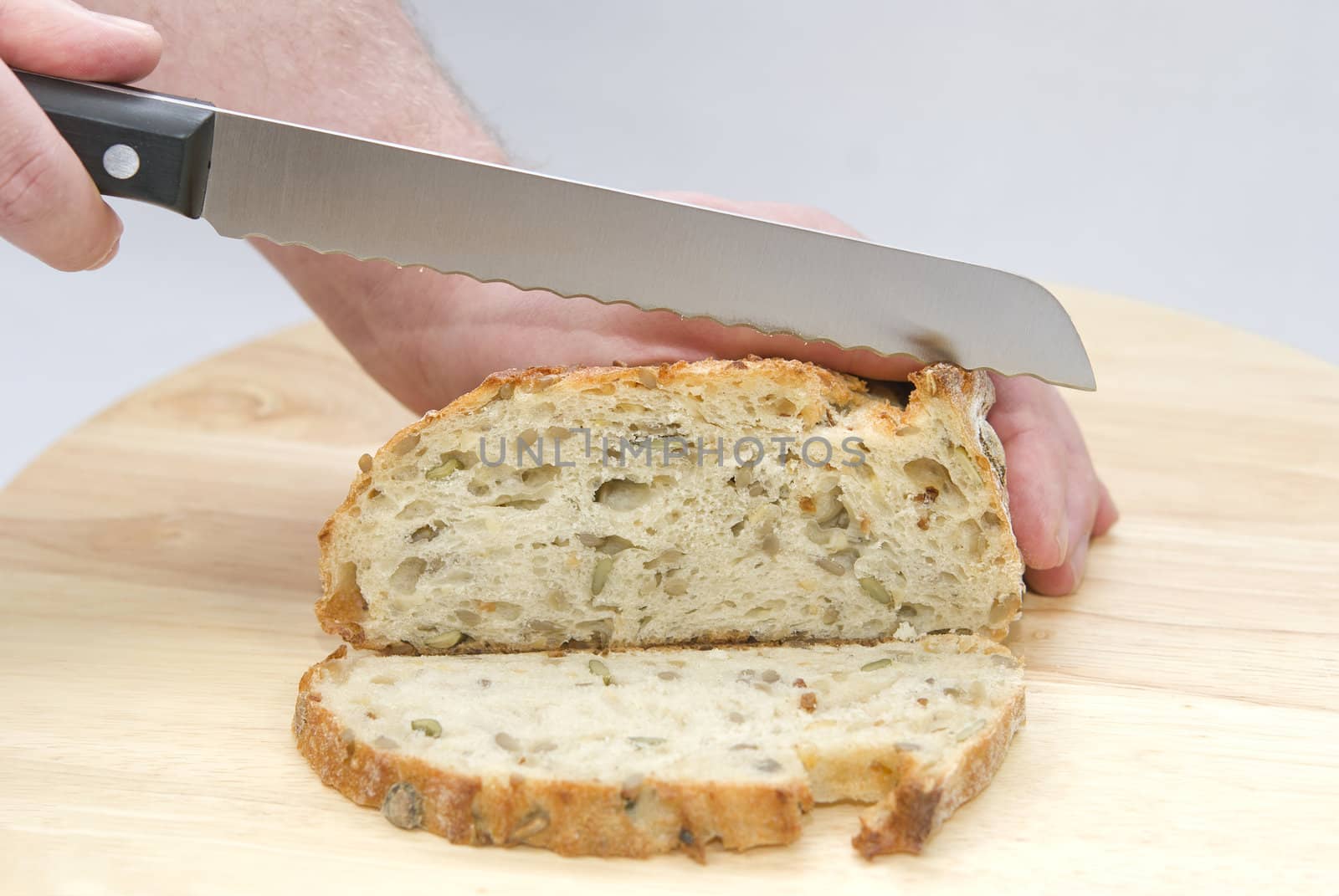 Human hands with a knife cutting a loaf of bread on the wooden board