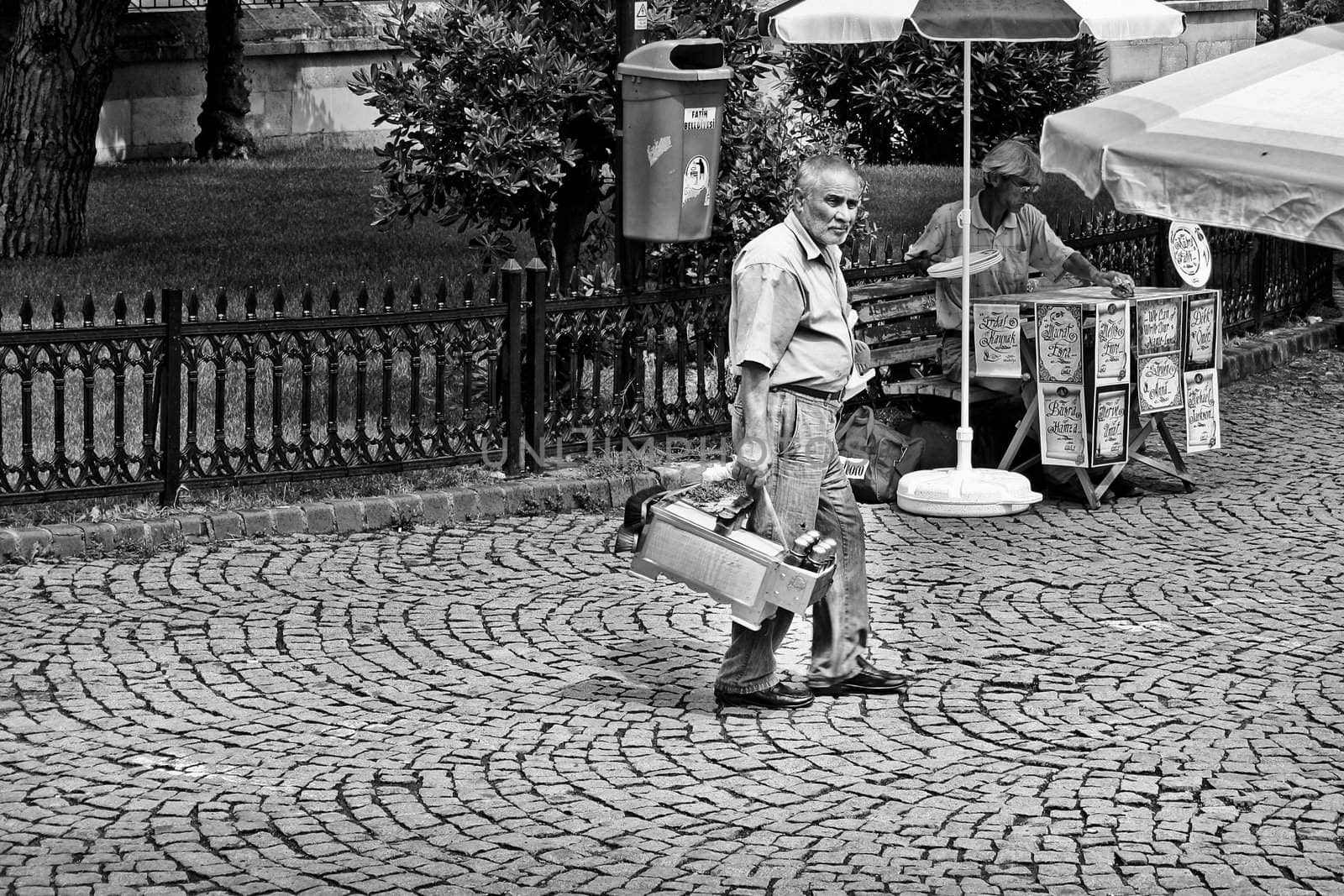 An old man carrying his shoe shine box and looking around for business