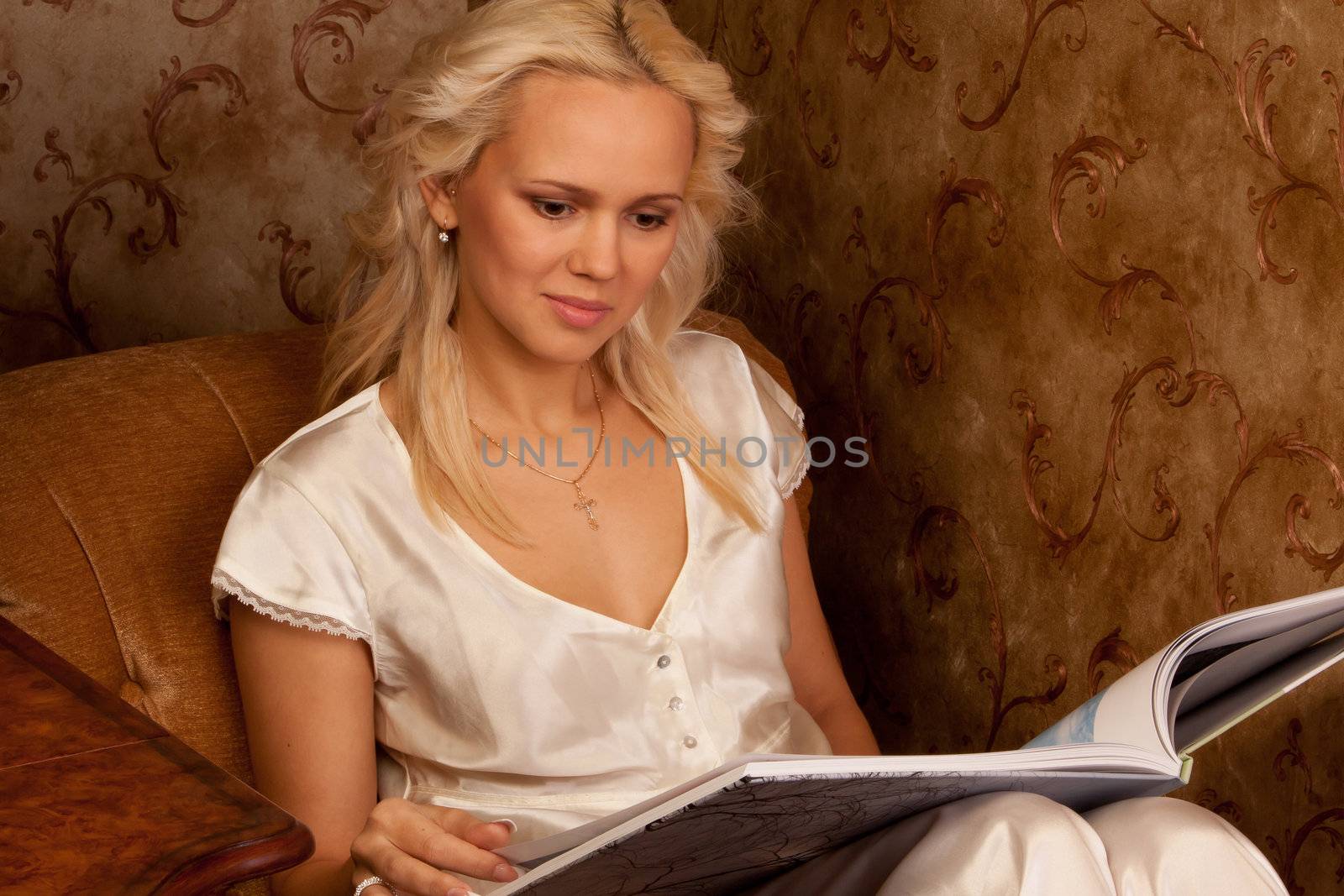 Young and beautiful girl reading a book cover in black sitting on a couch in his home