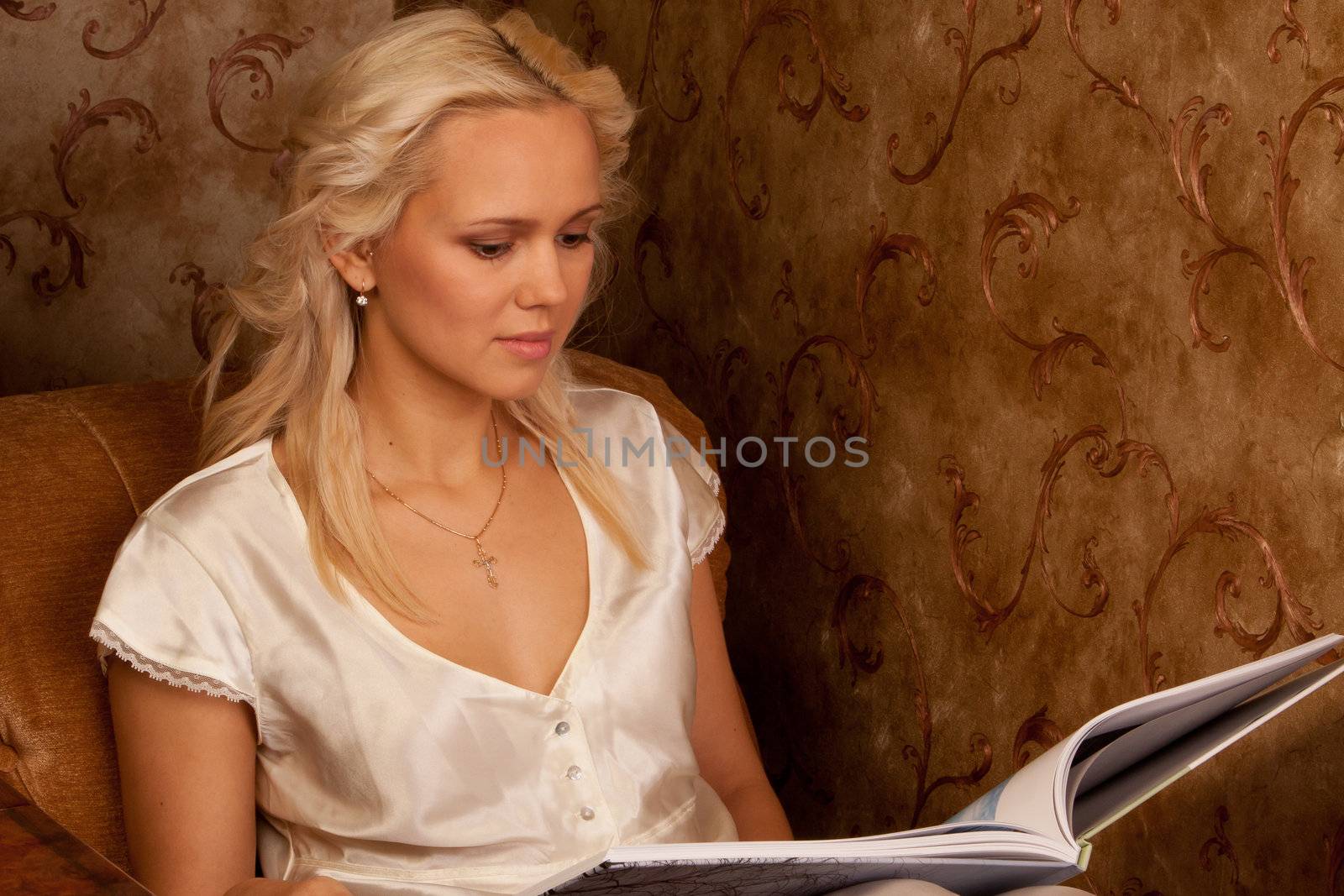 Young and beautiful girl reading a book cover in black sitting on a couch in his home