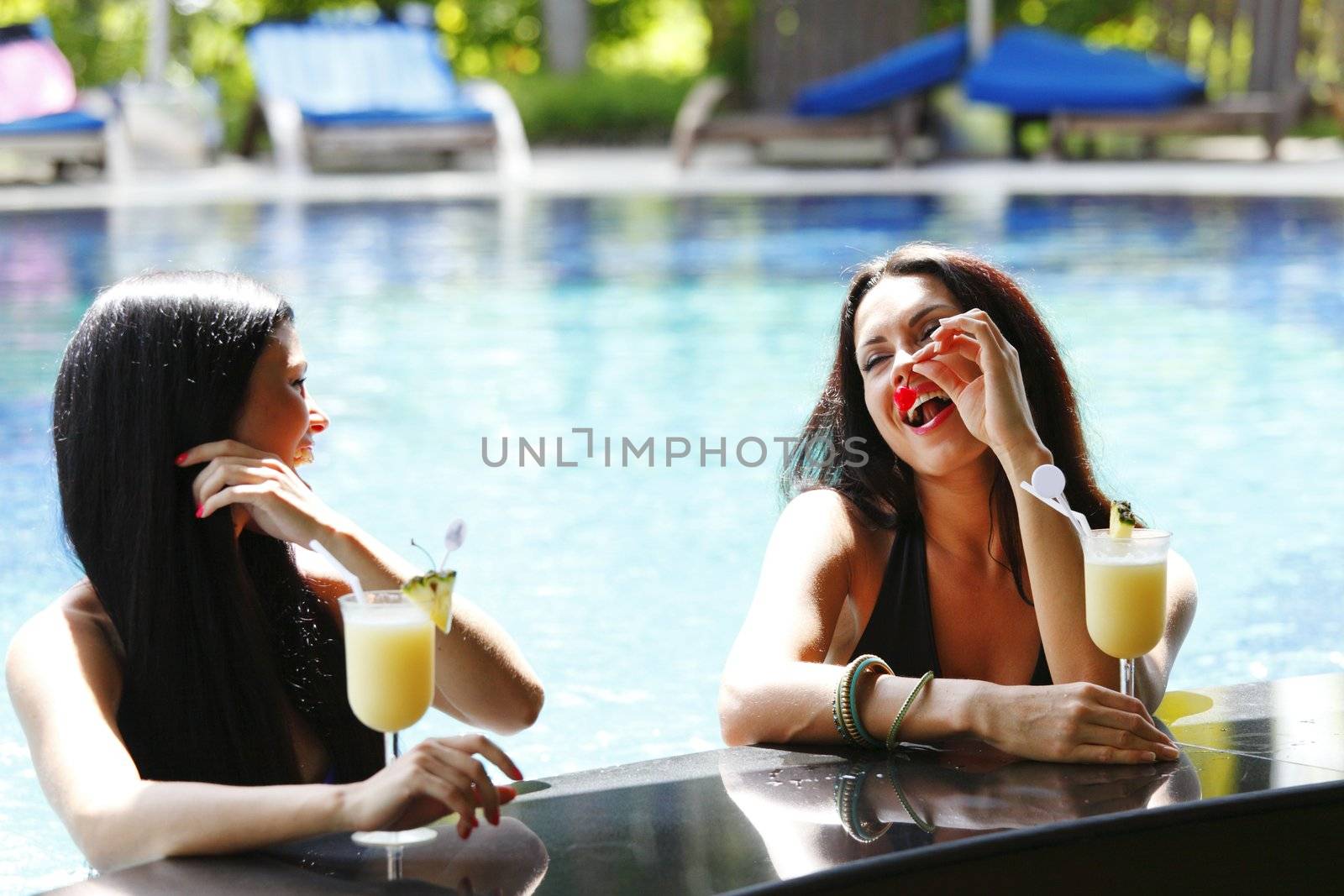 Two women with cocktails in swimming pool by Yellowj