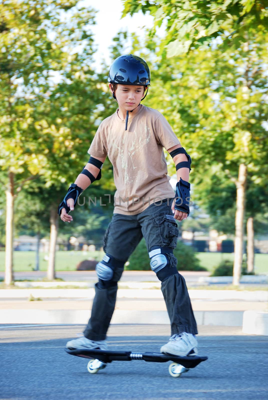 Teenage boy riding a skateboard in a parking lot with trees in the background on a sunny day.