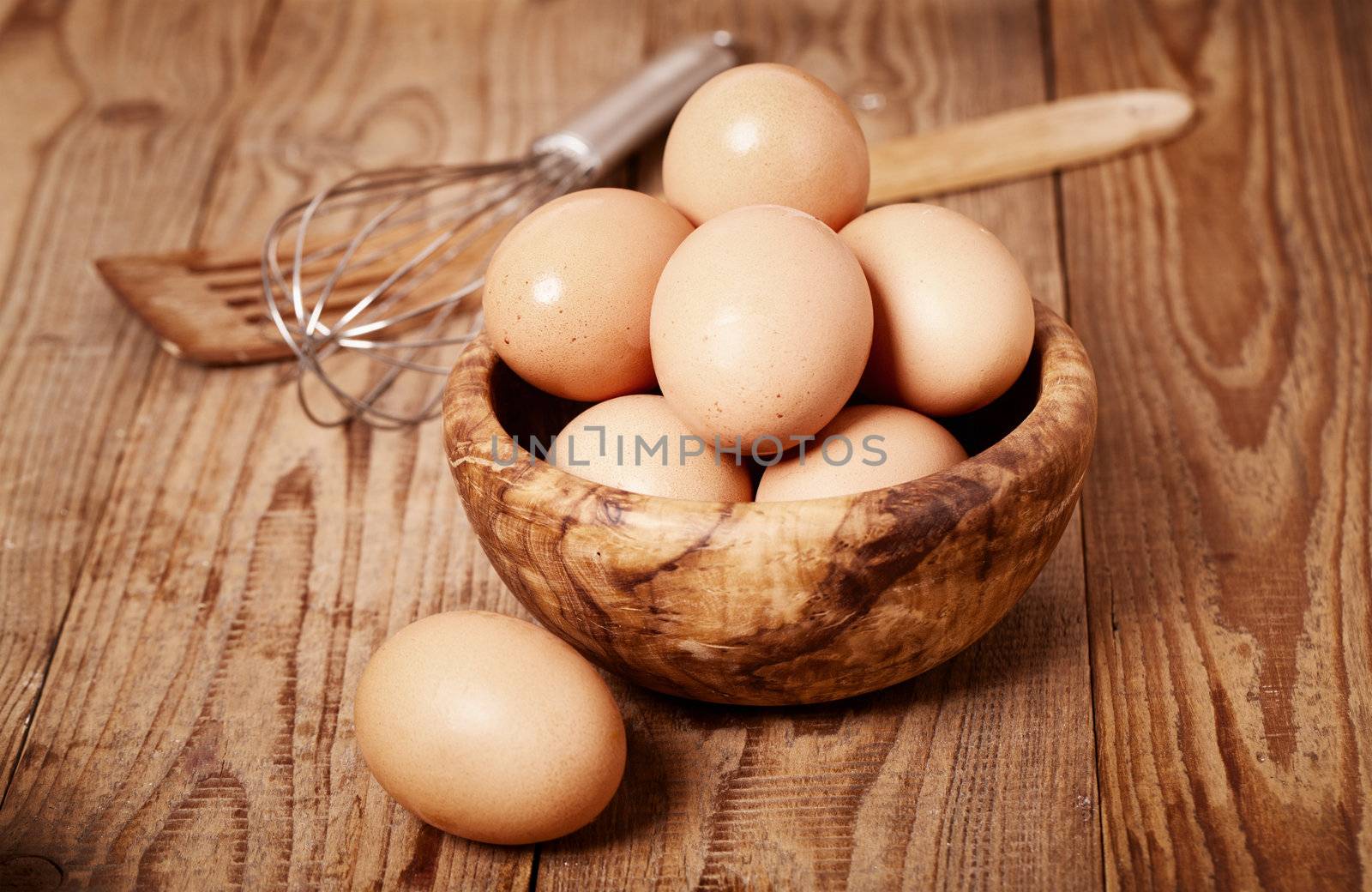 fresh brown eggs with egg whisk on wooden background by motorolka