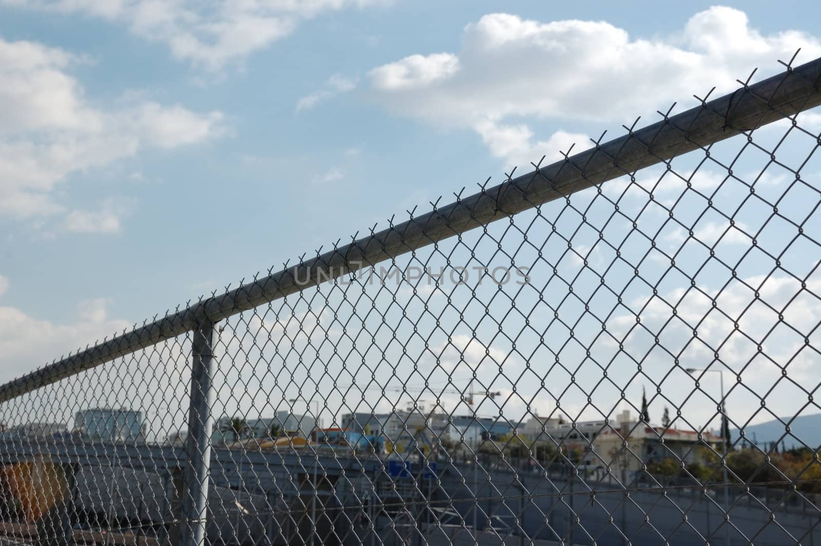 Cityscape through chain link fence. Highway barrier above the motorway.