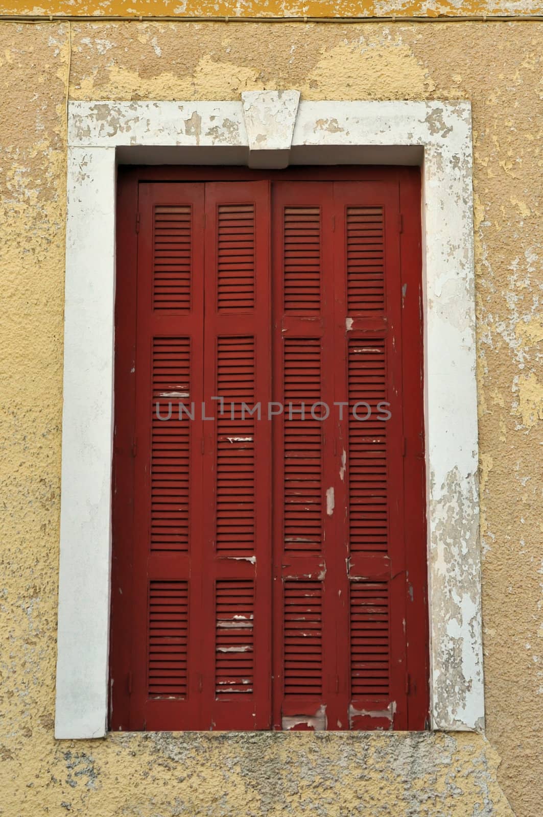 Red window shutter and weathered chipped paint wall.