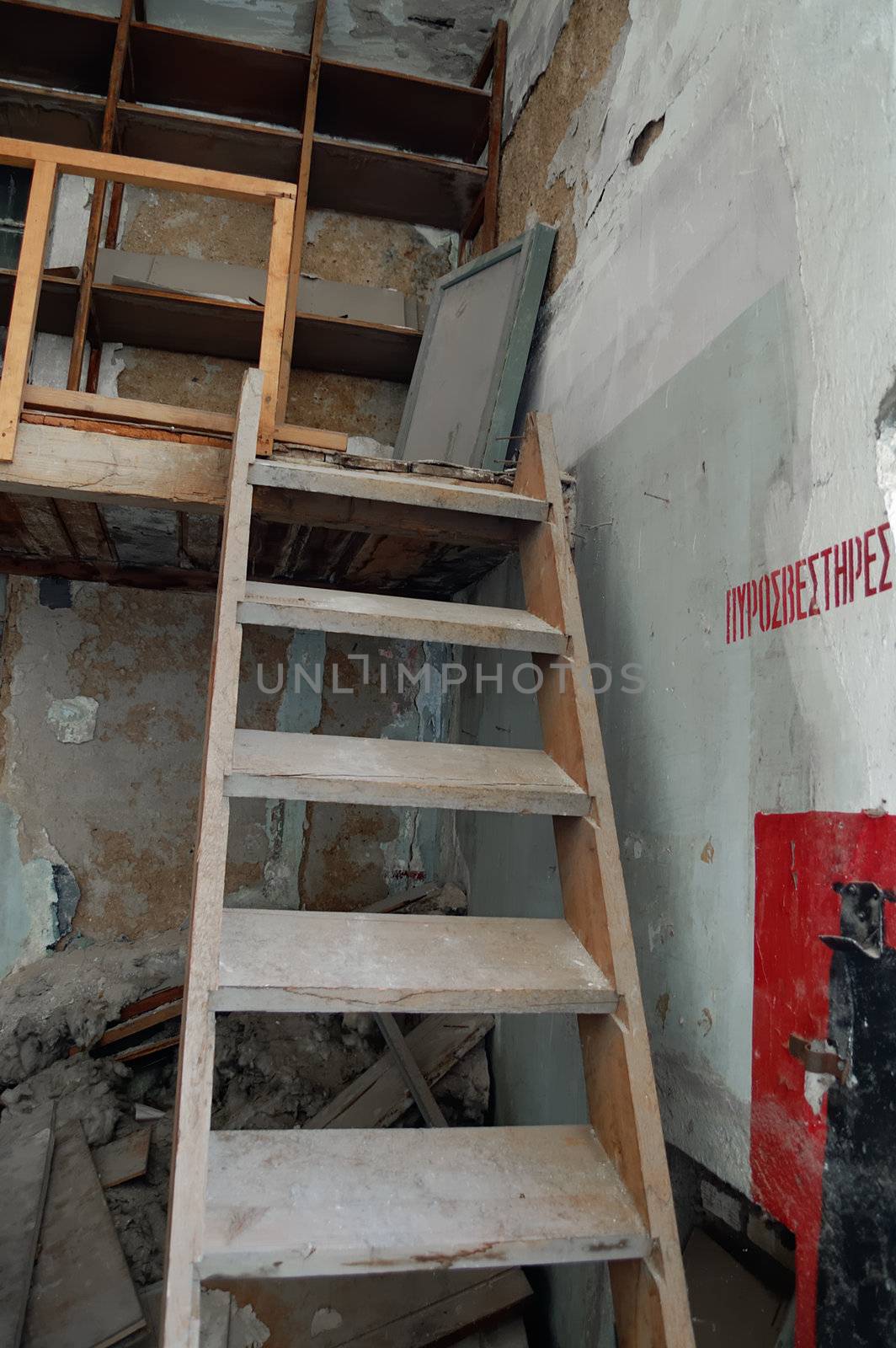 Steep wooden staircase crumbling attic and fire extinguisher sign in abandoned factory interior.