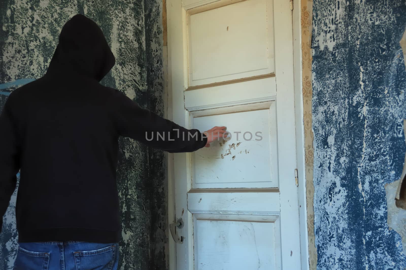 Ghostly hooded figure by the closed door of a decayed room. Abandoned house interior.