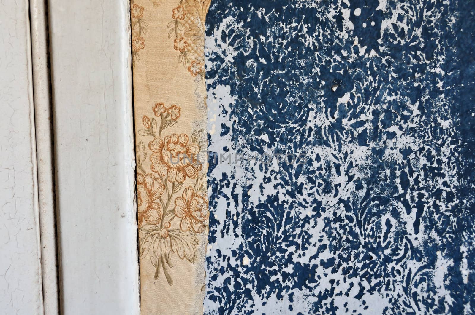 Torn vintage wallpaper and floral pattern imprinted on peeling paint wall.