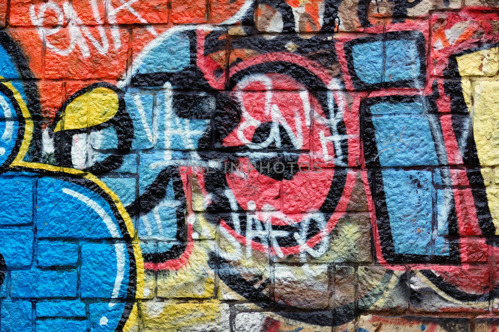 Wall with overlapping layers of messy graffiti and tags. Urban street art background.