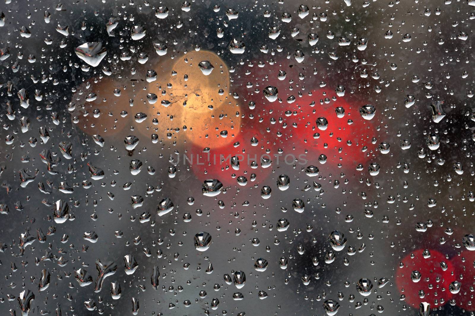 Raindrops on glass surface and blurry abstract city lights. Background texture.