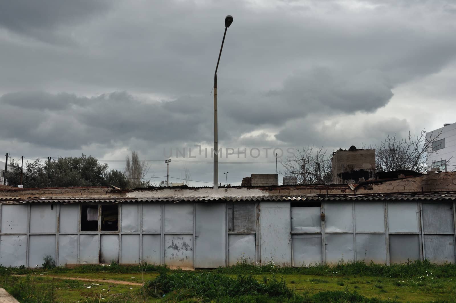 Rusty warehouse shack under moody sky. Street light emerging through the roof drying laundry by the window.