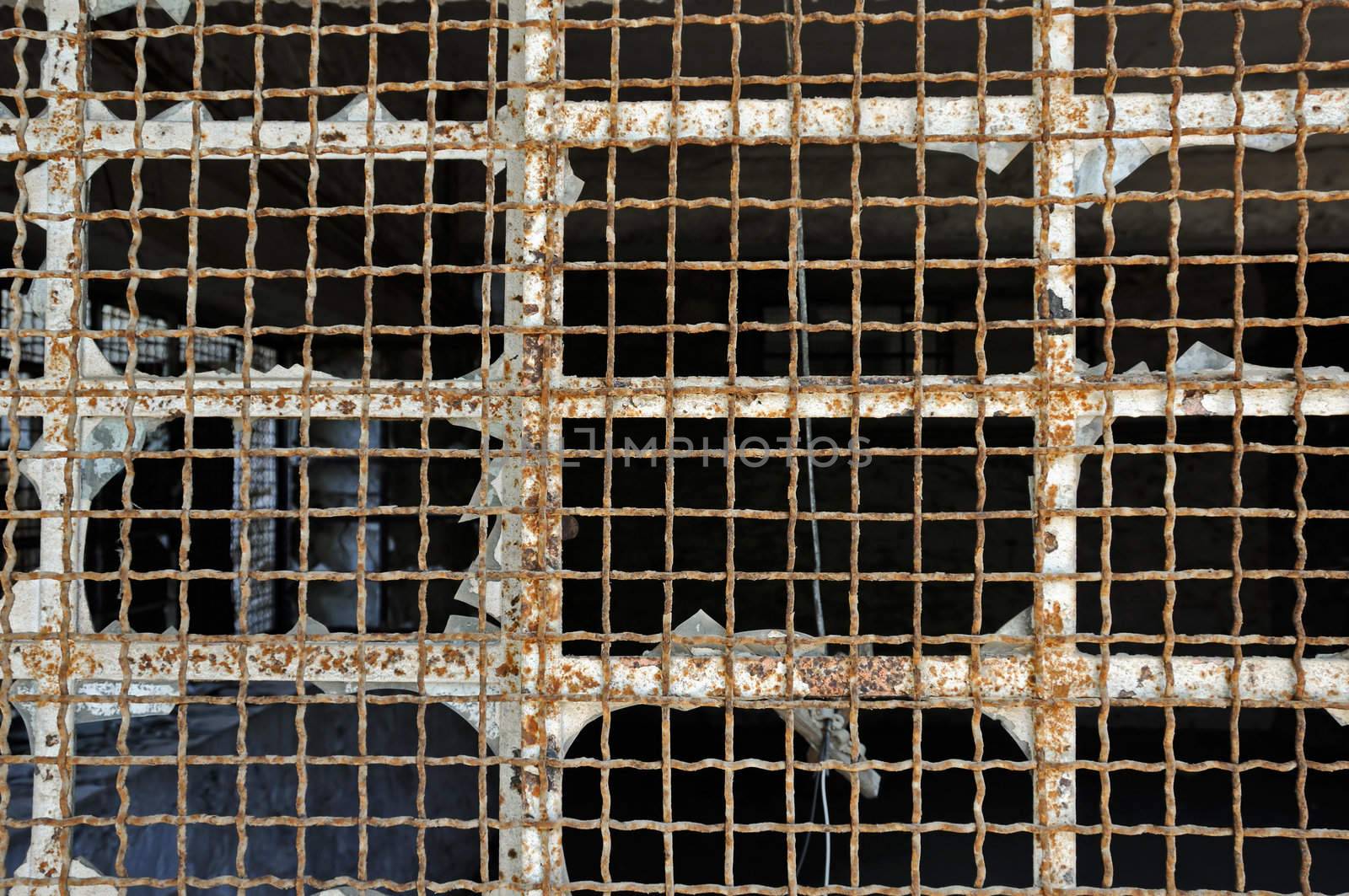 Broken industrial window wire mesh in abandoned warehouse. Rusty metal texture.