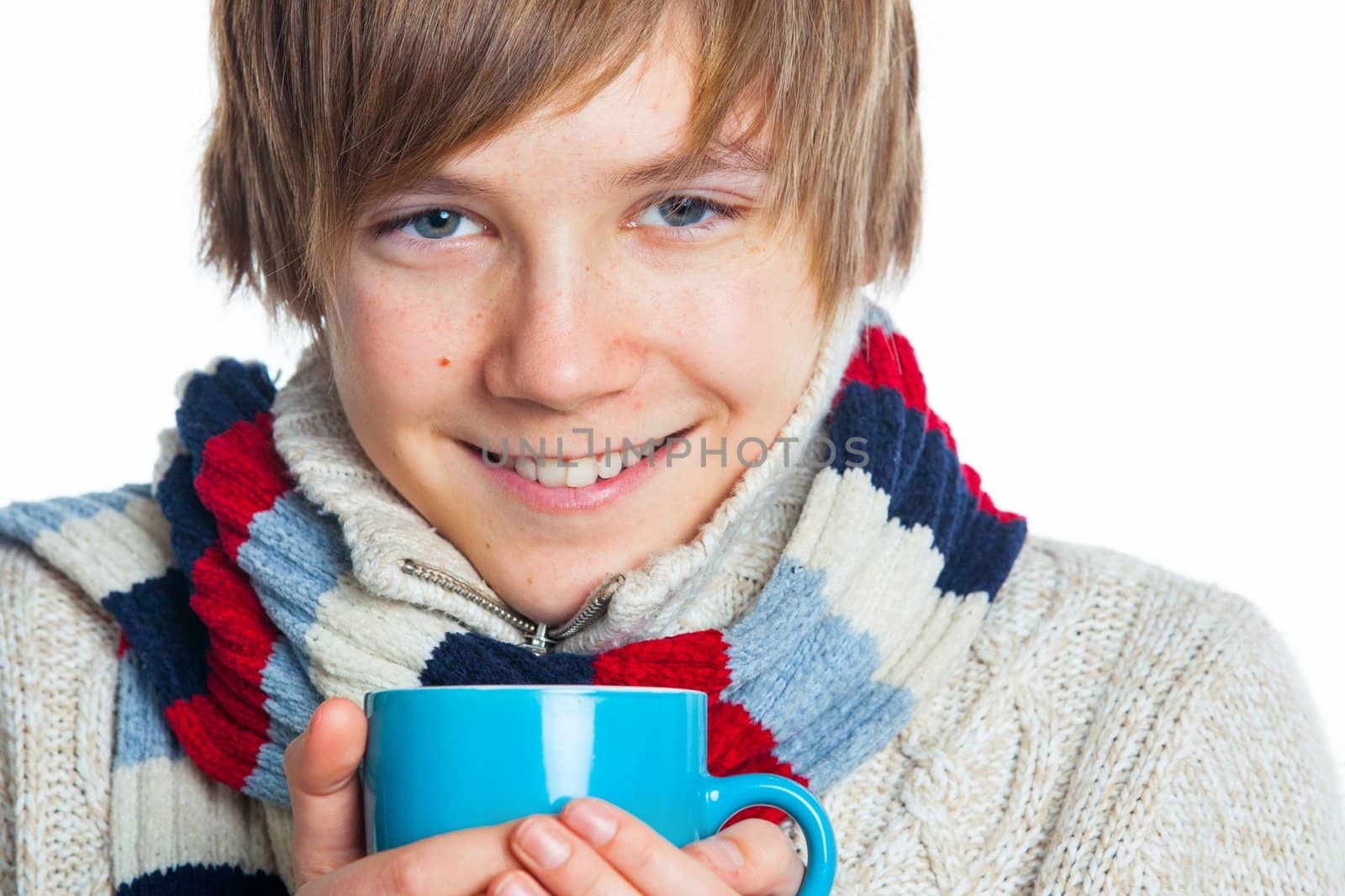 Portrait of young smiling cute frozen teenager in a scarf and with blue cup, isolated on white