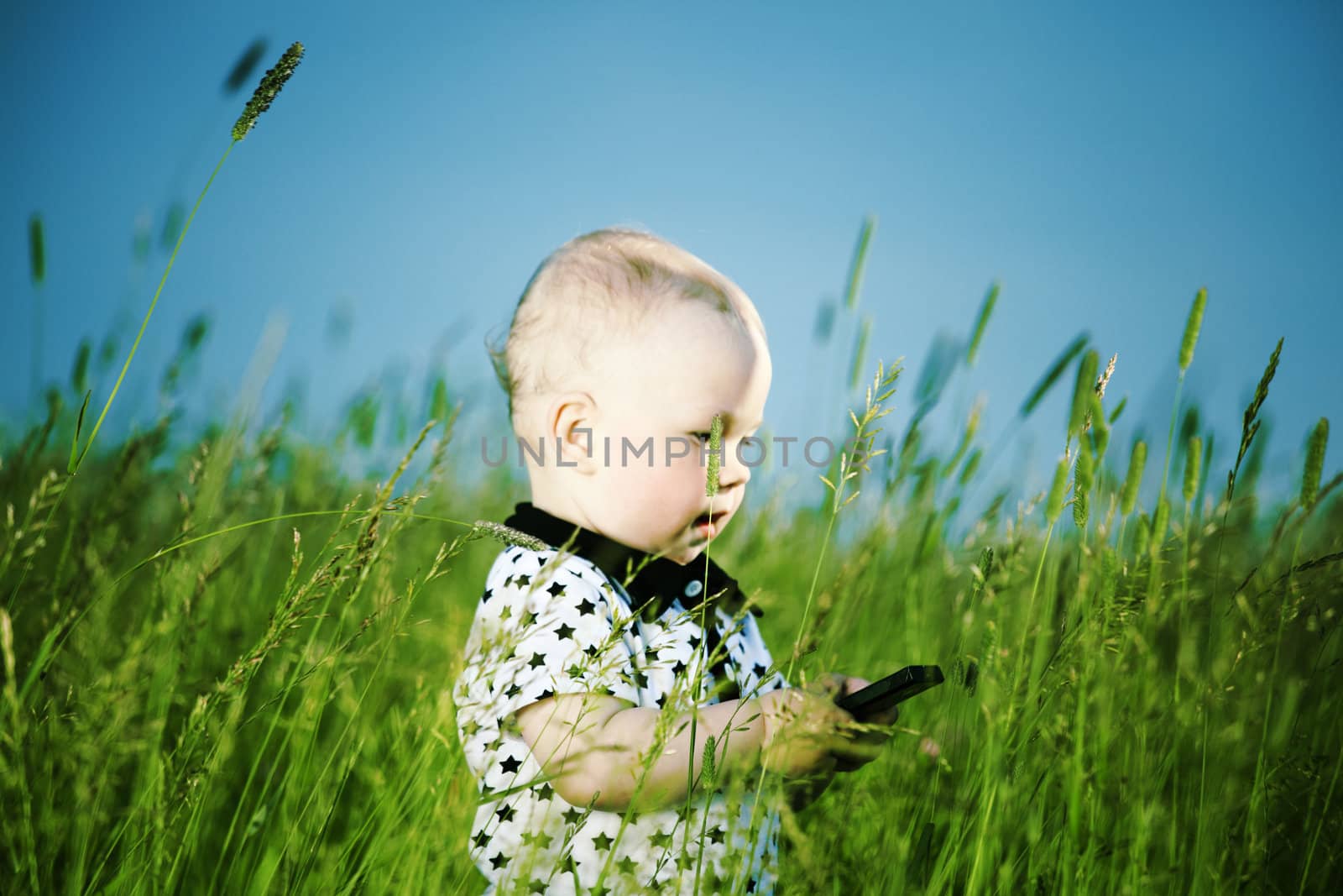 little boy in green grass call by phone