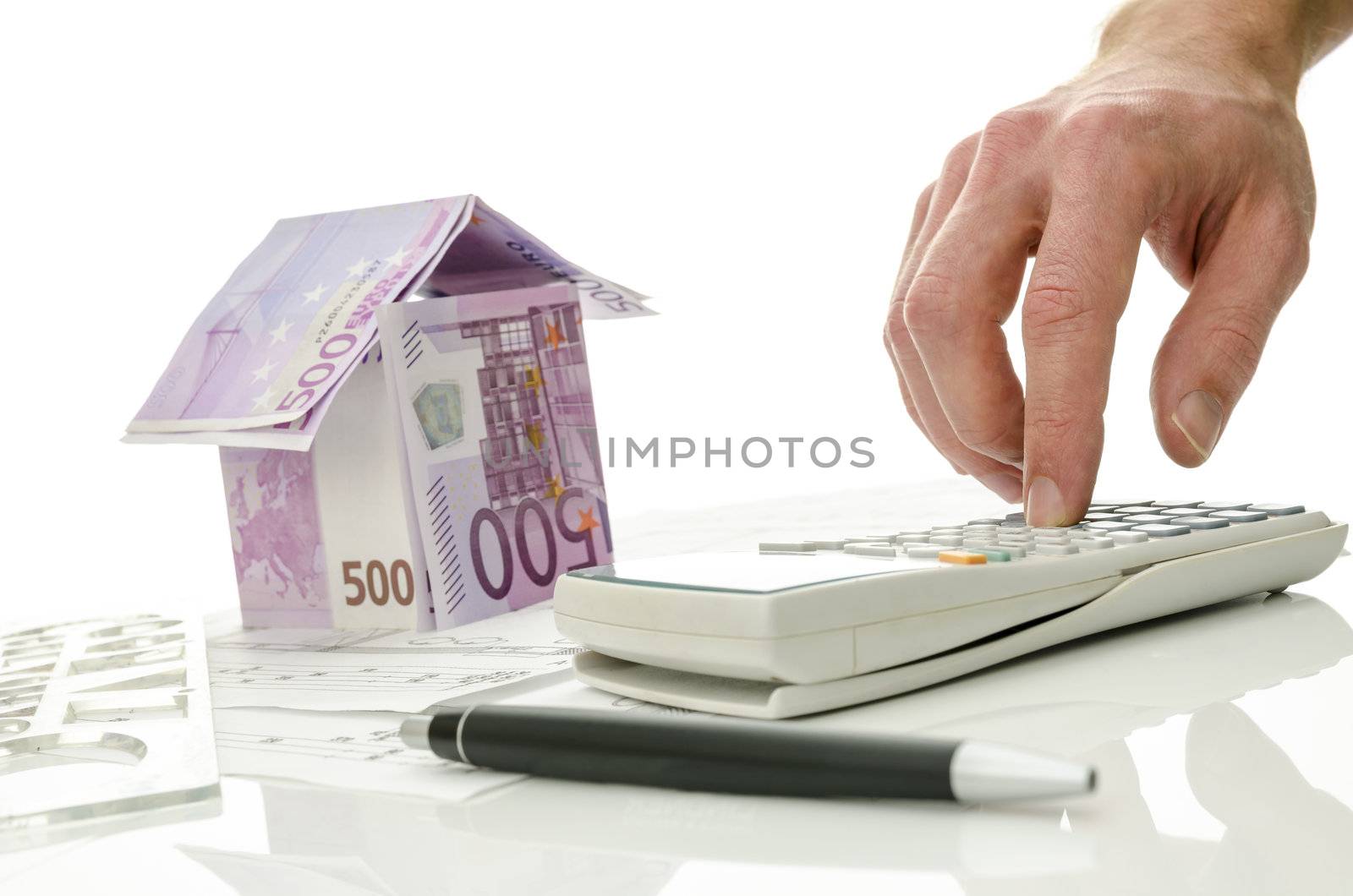 Contractor calculating costs of a house. House made of Euro money in background. Focus on a hand.