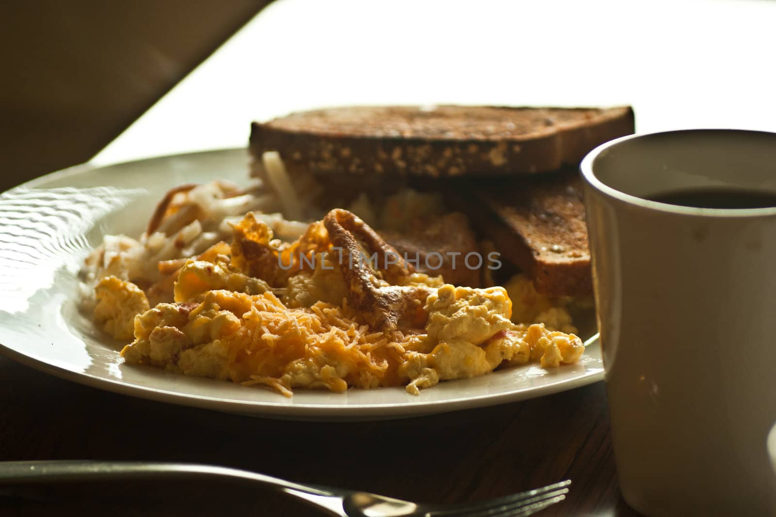 A full view of a plate of breakfast food ready to eat with coffee cup in forground.