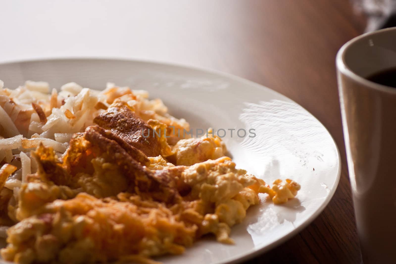 A croped view of a plate of breakfast food ready to eat with coffee cup in forground.