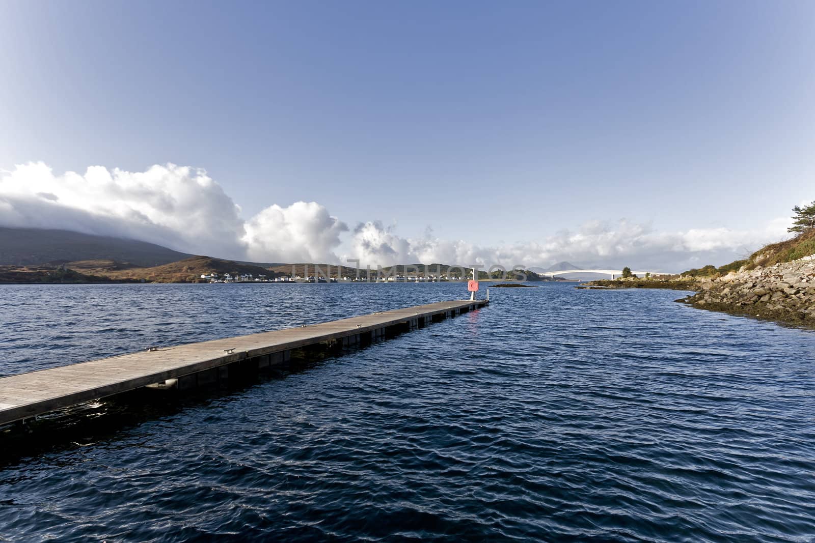 long peer in scottish bay with hills in background and blue sky