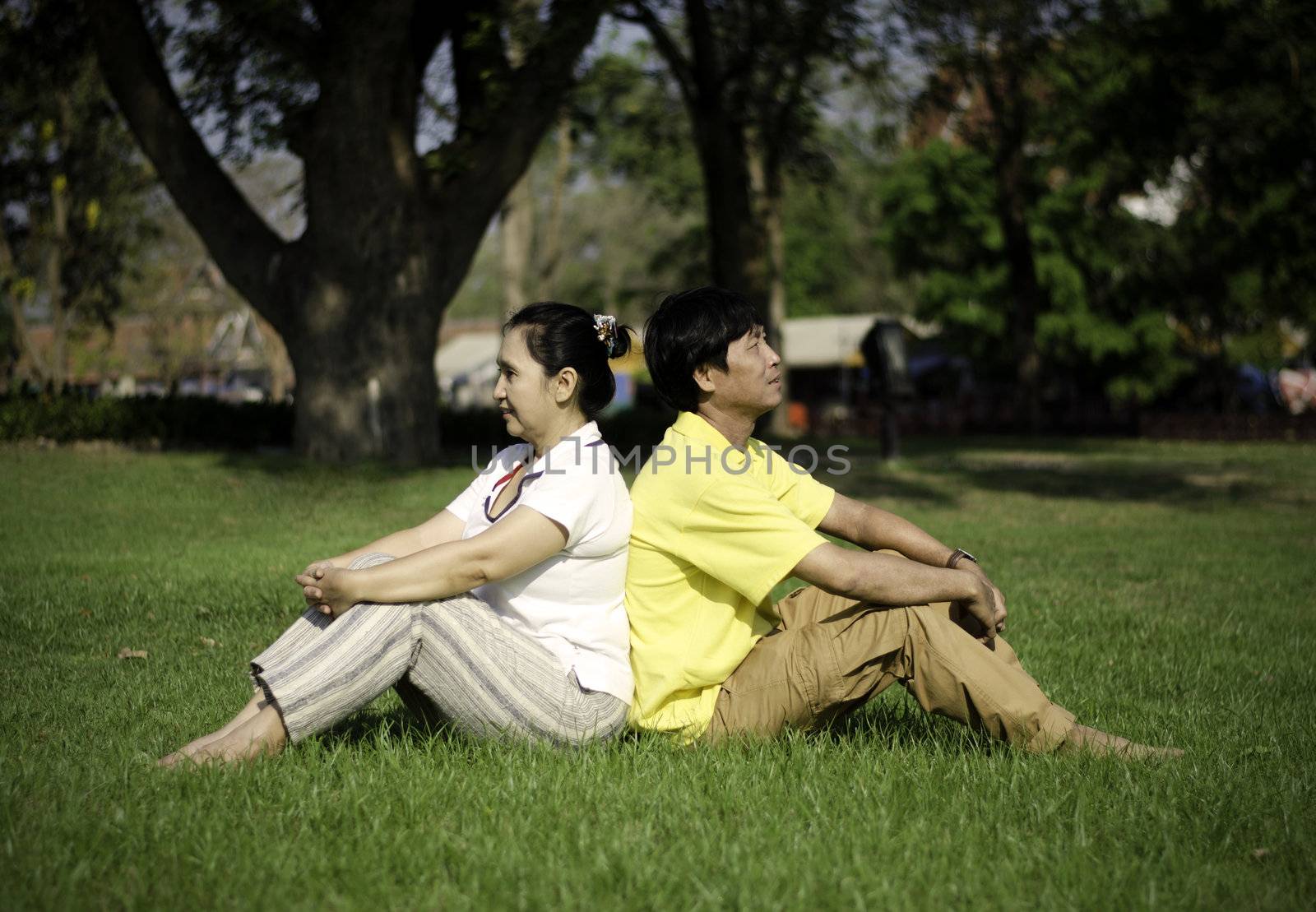 Portrait of beautiful couple sitting on ground in park by siraanamwong