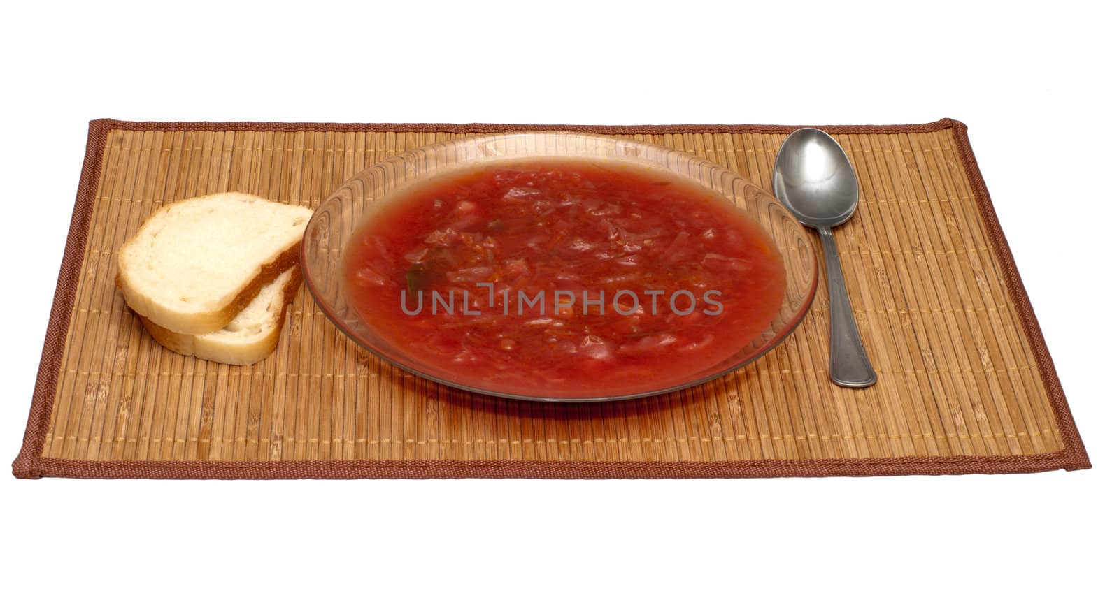 Plate with a borsch and bread on a bamboo mat.